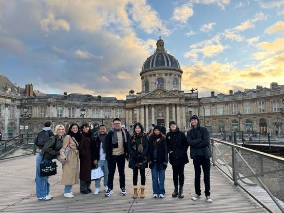 Students in Paris A group of people stands on a bridge, with a large building visible in the background.